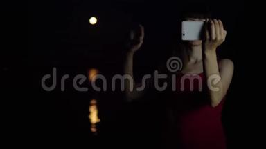 一个年轻的女人用智能手机相机对着红月自拍。